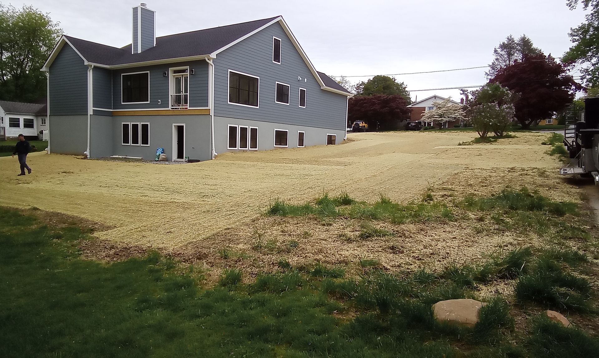 Gray house with a large gravel yard and green grass in front, under an overcast sky