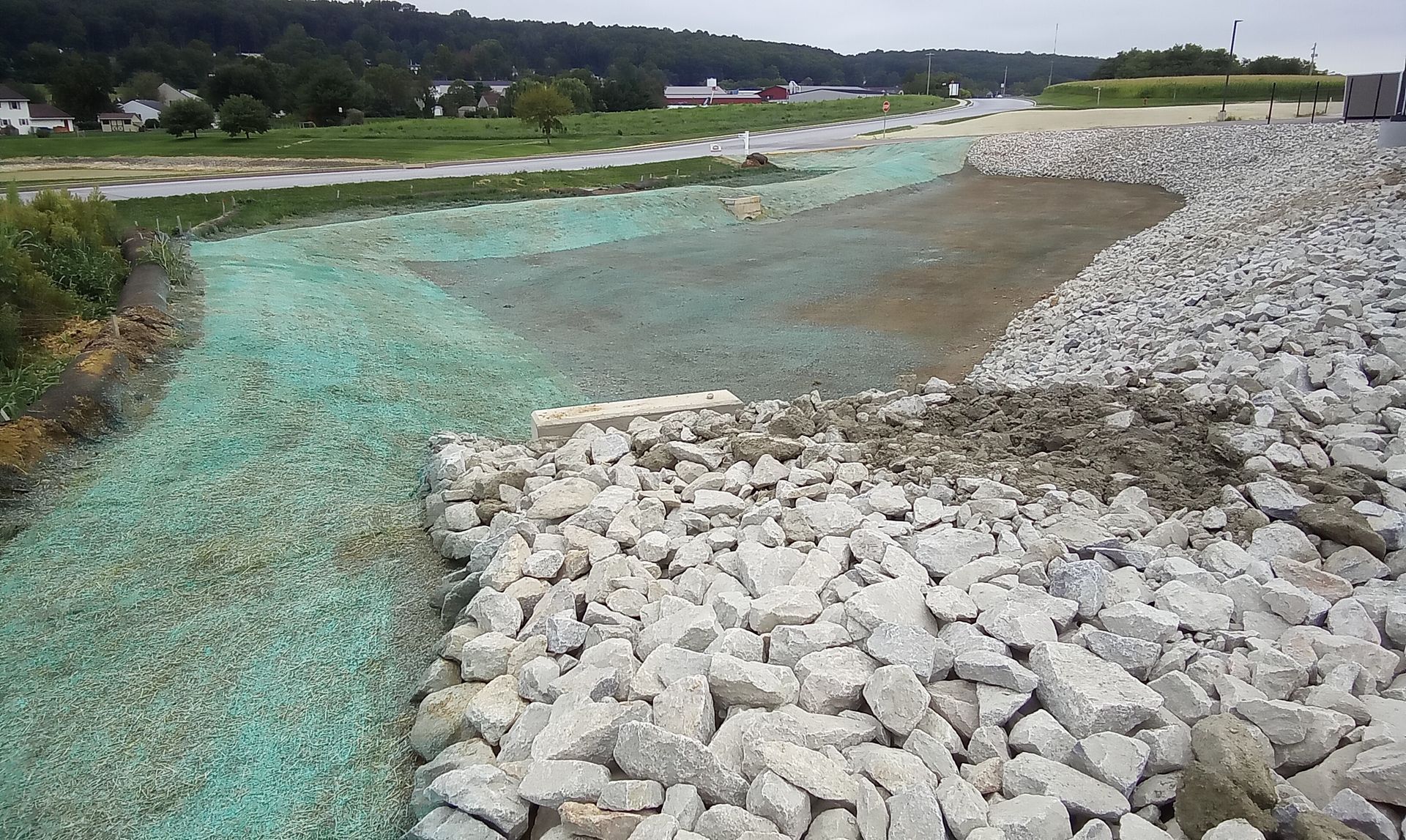 Rock-covered riverbank with turquoise water flowing through a rural landscape.