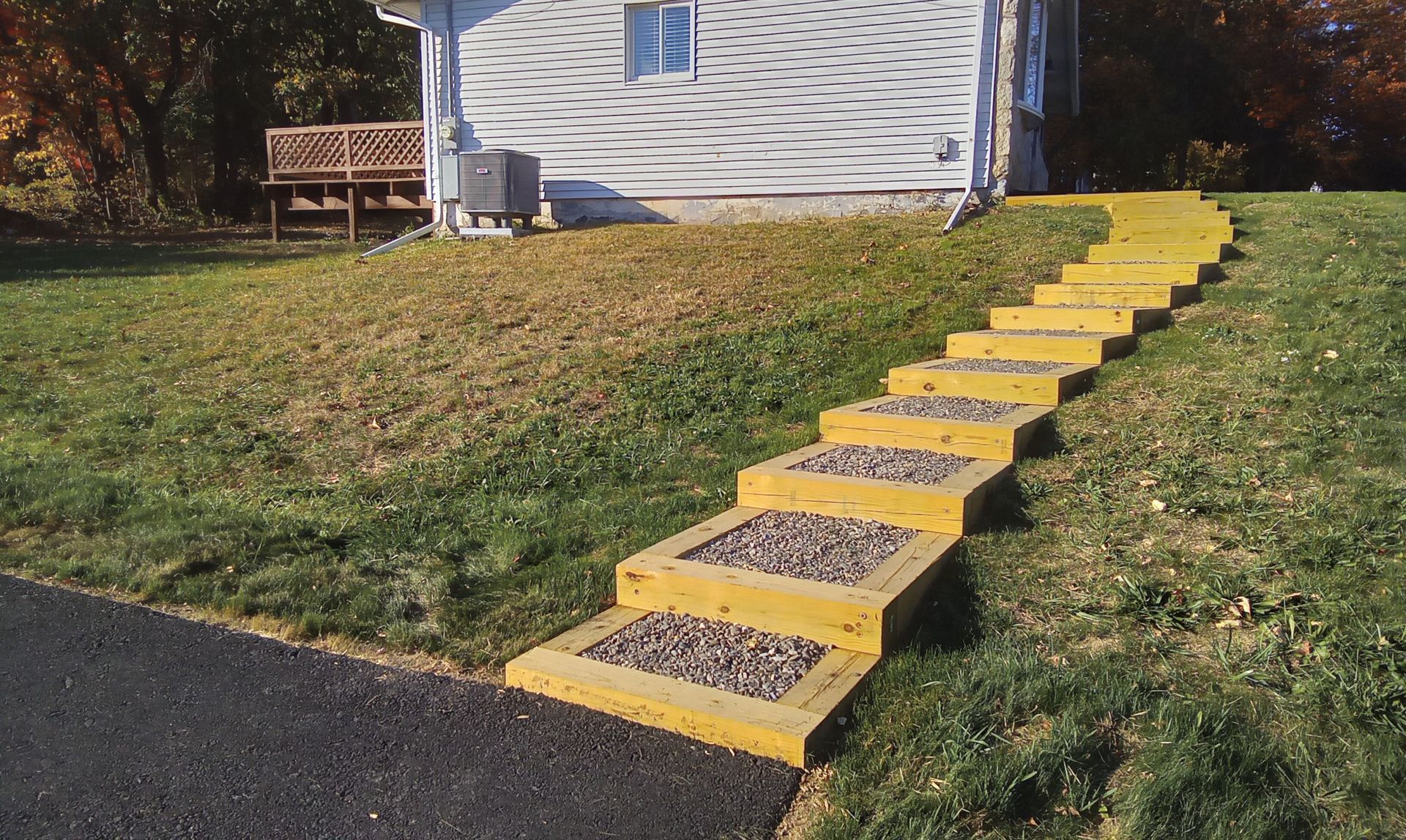 Yellow-edged concrete steps up a grassy slope beside a house, leading to a white wall.