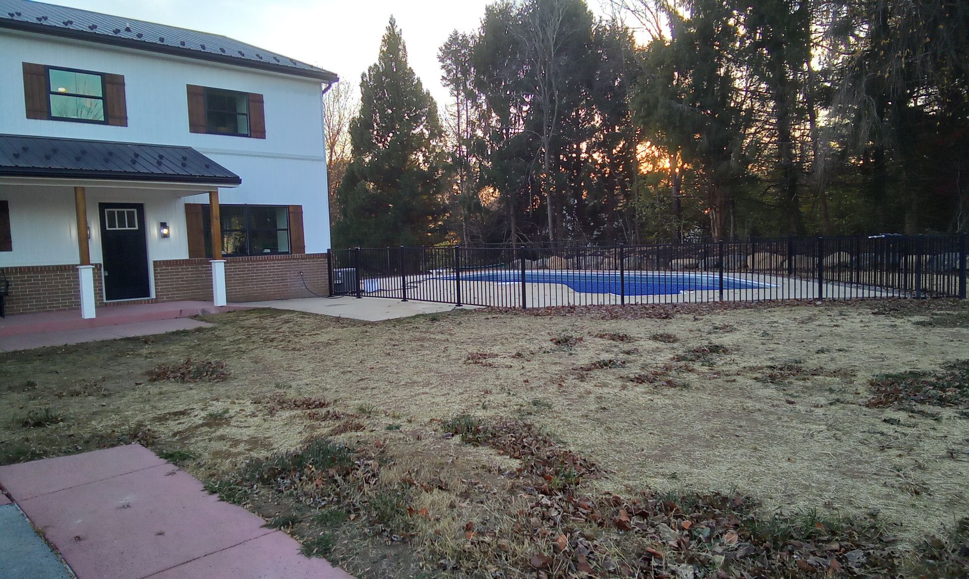 Two-story house with a fenced backyard, bare grass, and a pool at sunset
