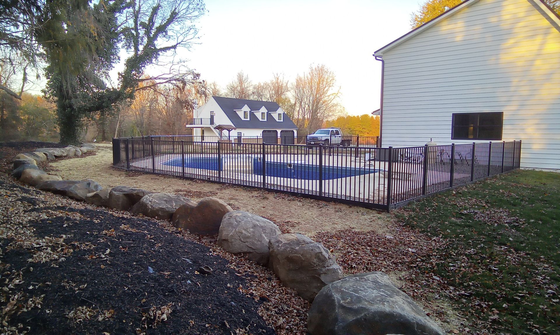 Backyard with black fence, stone border, and white house in autumn light