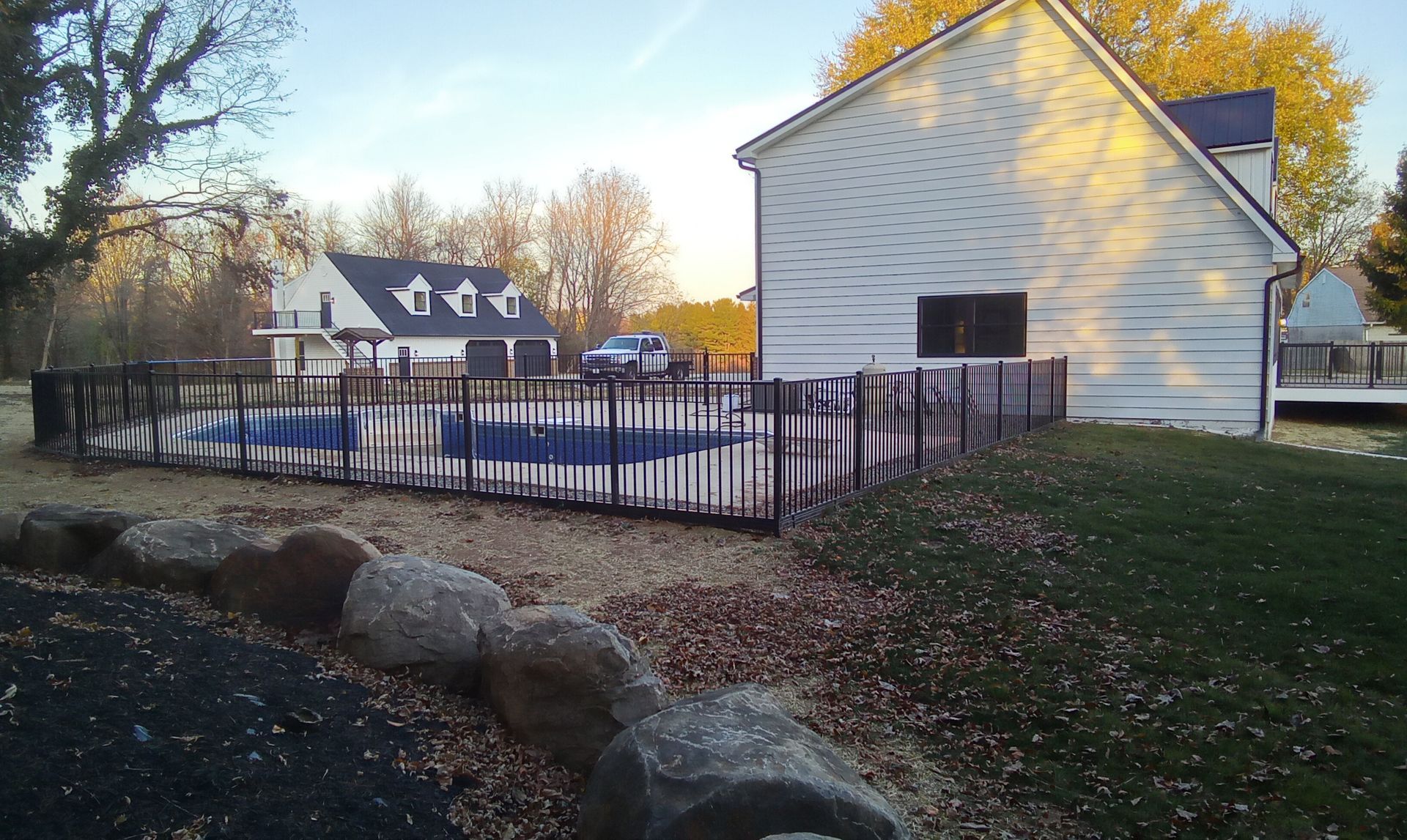 White house with black fence beside a pond and large rocks in a sunny yard.