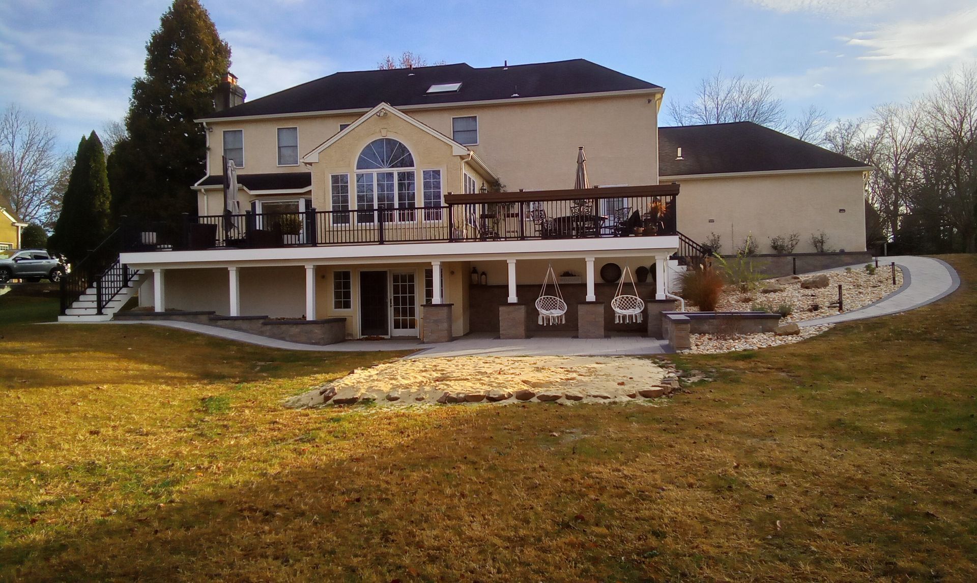 Large cream-colored house with a covered patio and balcony on a grassy hillside at sunset