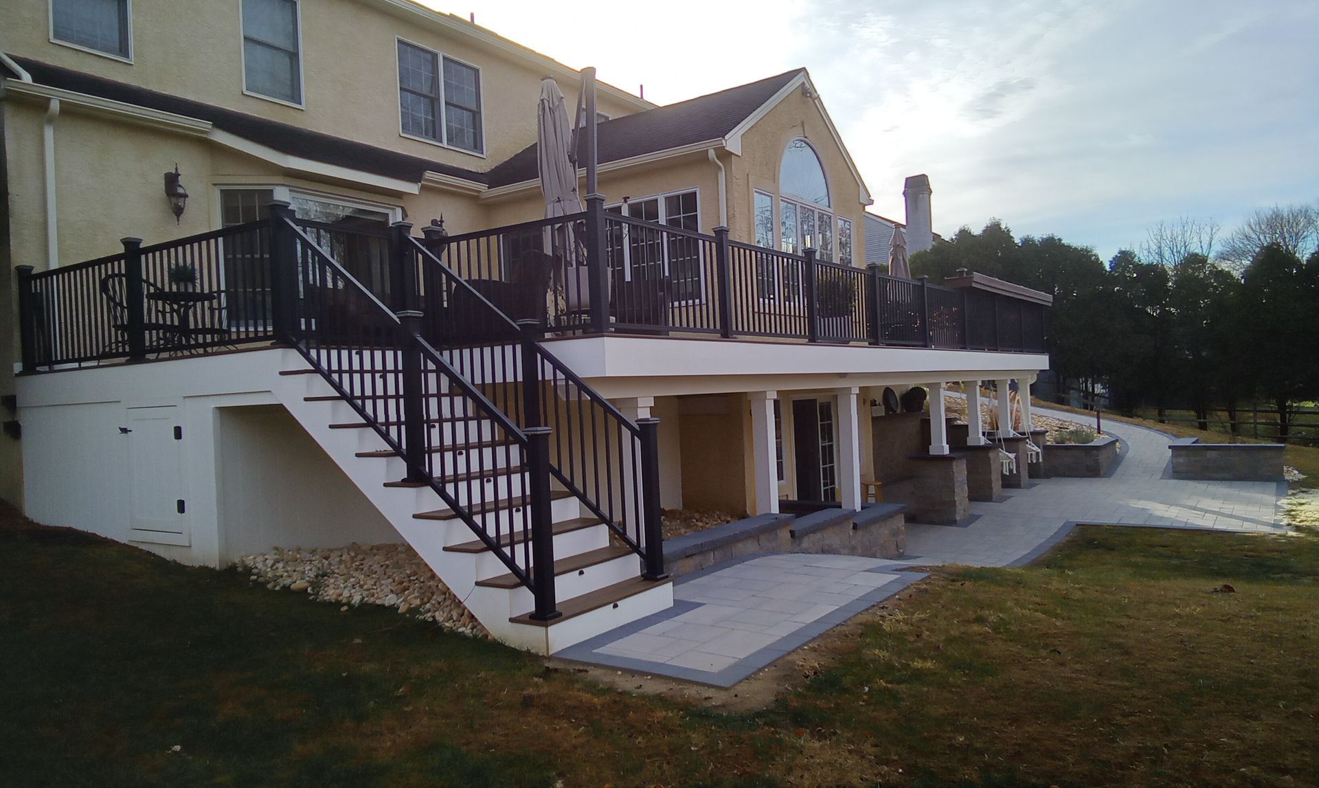 Two-story house with beige siding, black stairs and deck overlooking a grassy yard at sunset