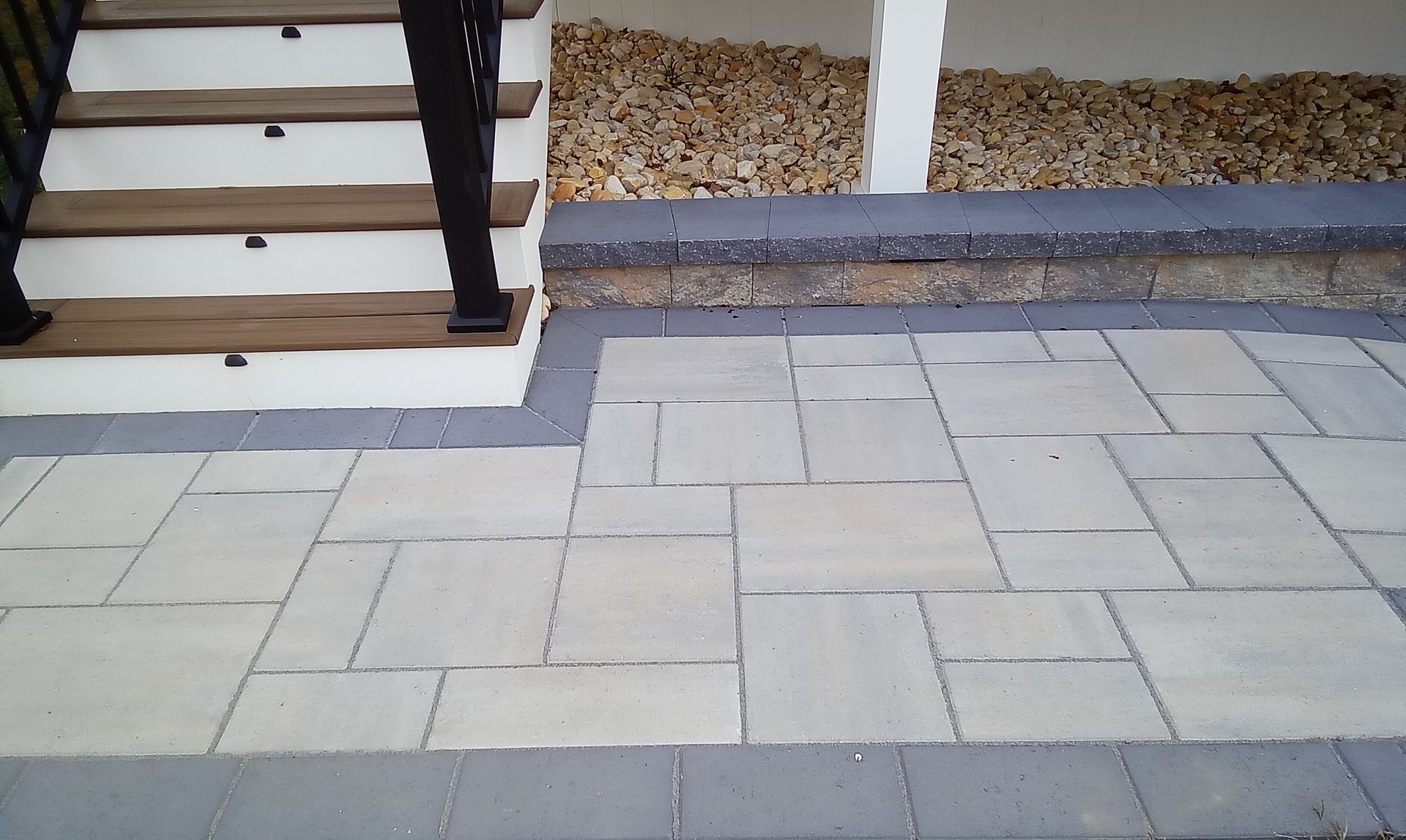 Paved walkway with light stone pavers and dark edging beside stairs and a gravel bed