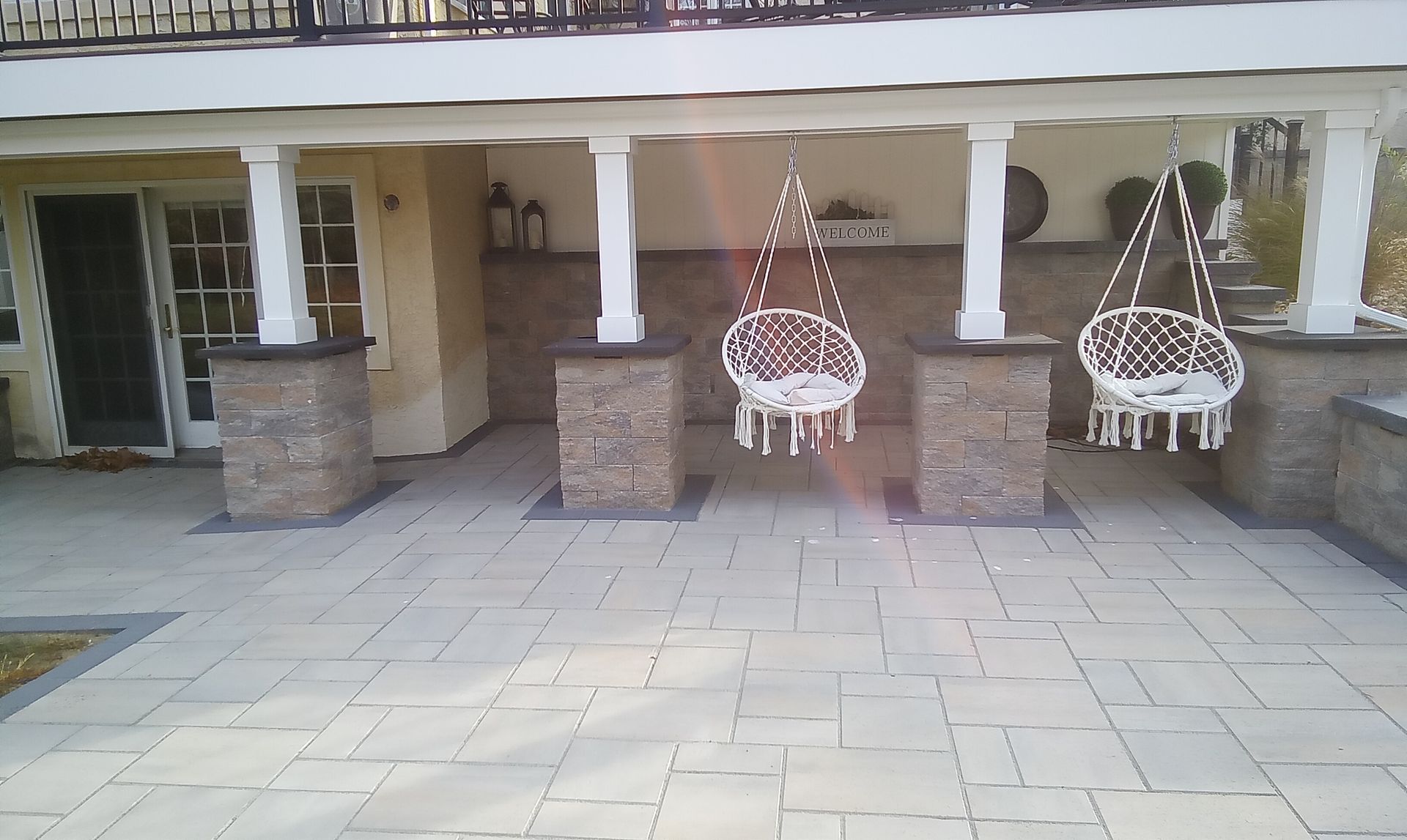 Covered patio with stone columns, tiled floor, and two hanging white chairs.