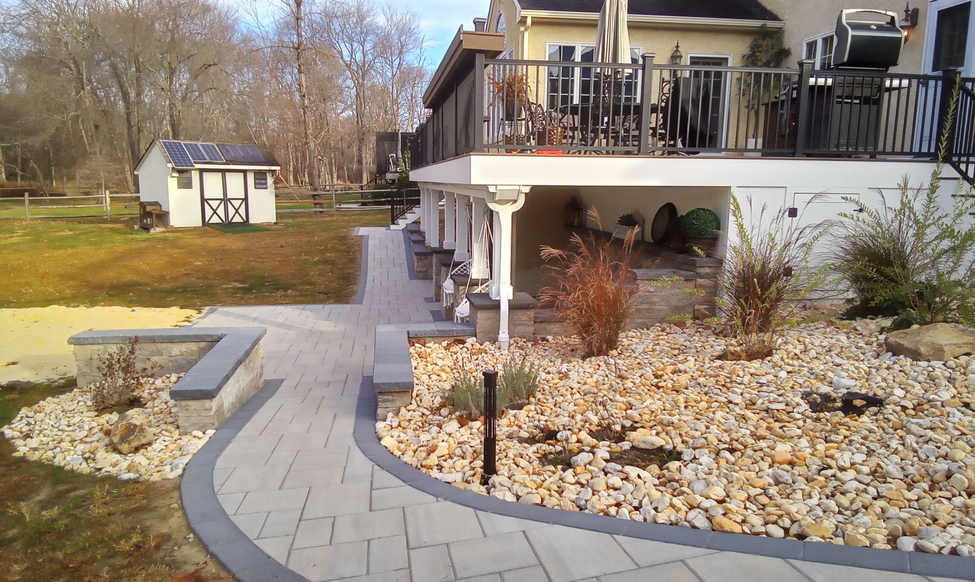 Backyard patio with stone pavers, rock landscaping, and a two-story deck beside a small shed.
