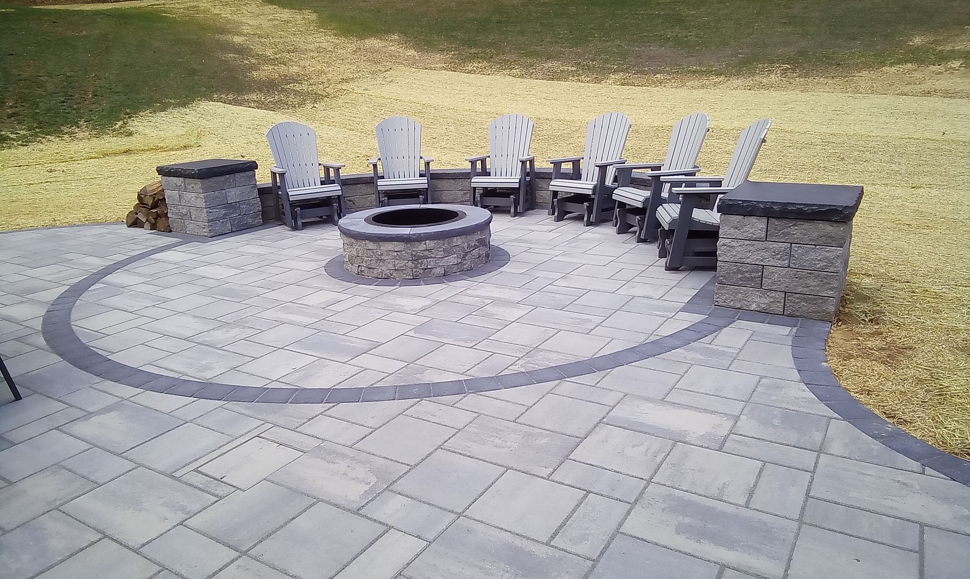 Circular stone patio with built-in fire pit and curved benches in a grassy backyard