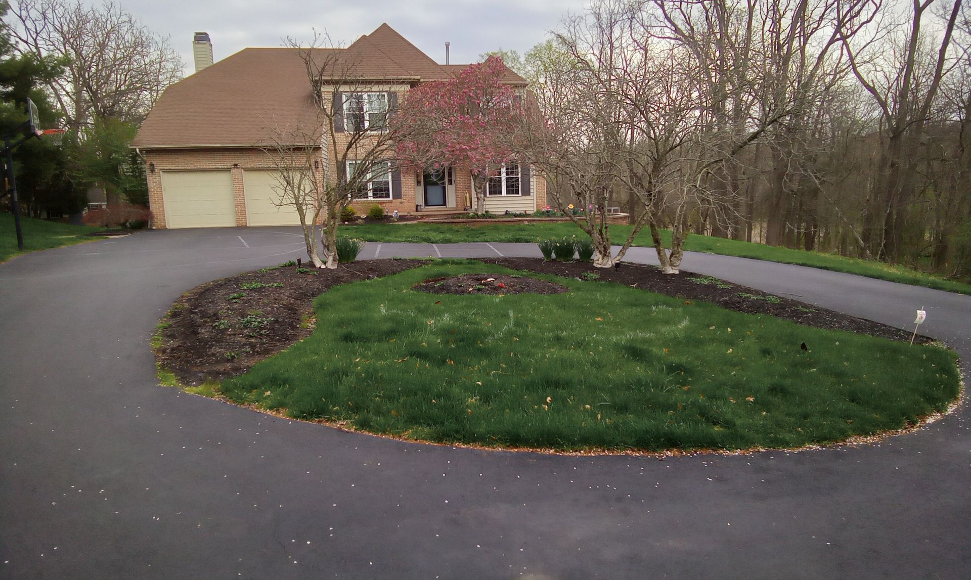 Suburban driveway curving around a grassy island with trees in front of a house