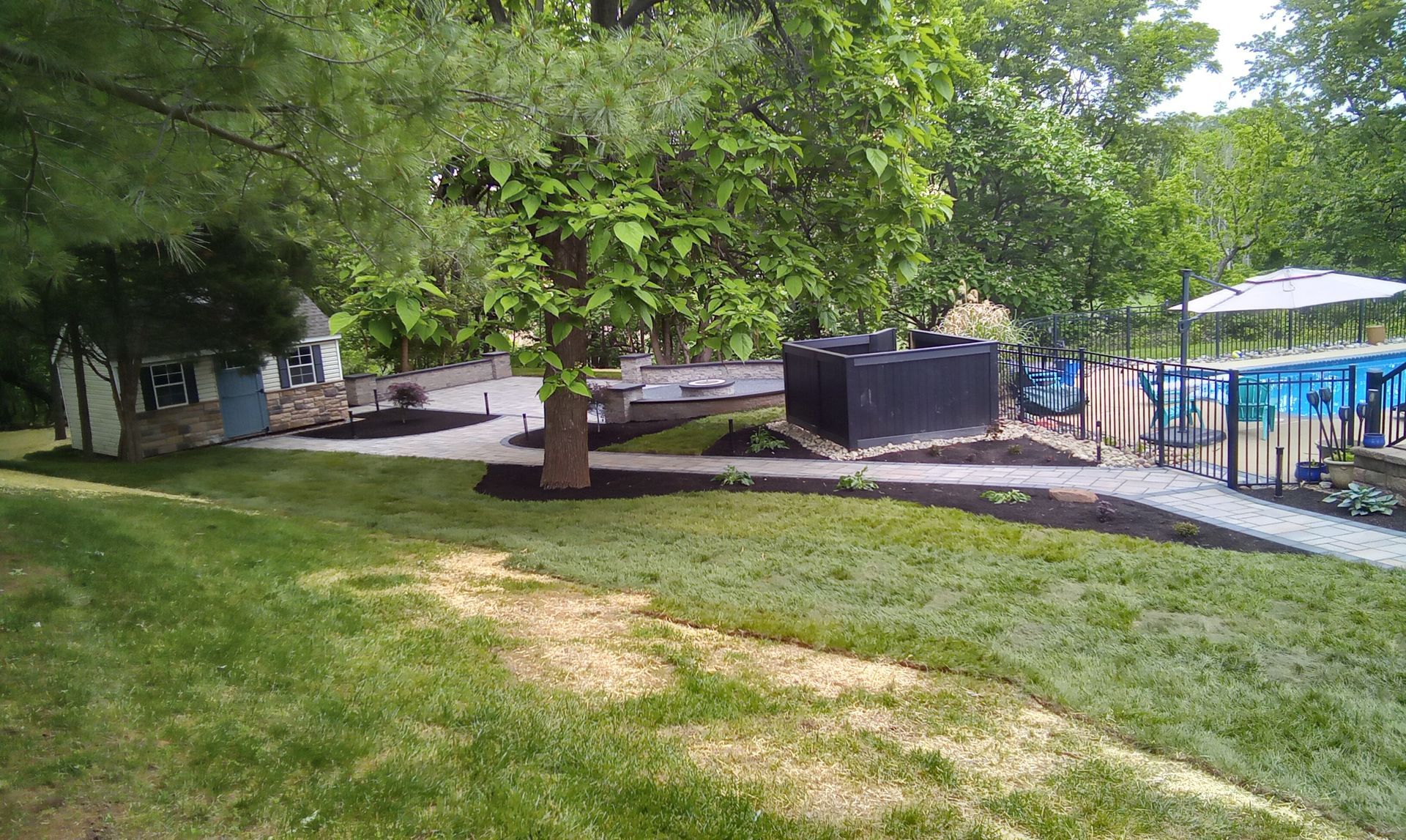 Shaded park lawn with a large tree, walkway, and a fenced blue pool area in the background