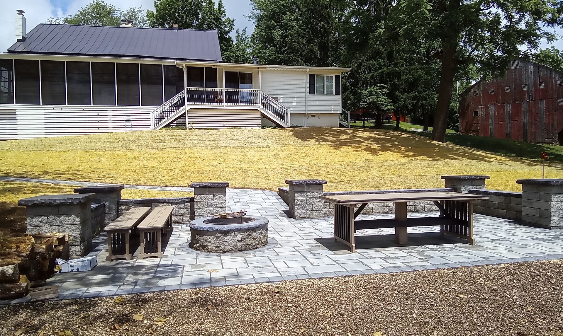 Outdoor patio with stone benches and picnic tables in front of a house, covered in yellow leaves