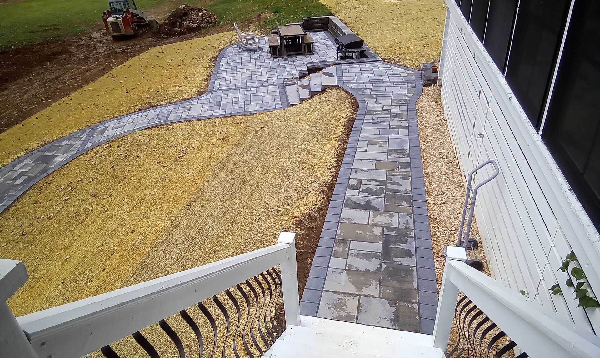 Curved stone walkway through yellow mulch beside a white house, viewed from a porch