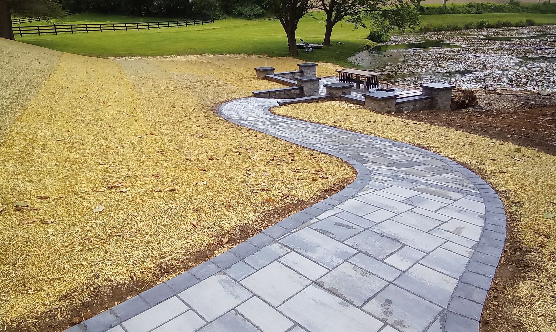 Curving stone walkway through a yellow-leaf park toward outdoor tables under trees