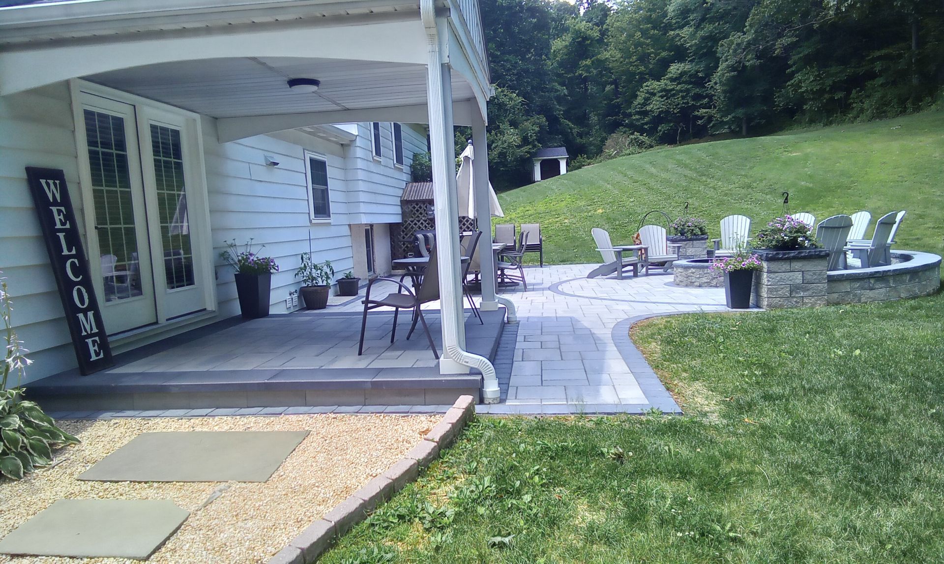 Back patio with white chairs, stone path, and green lawn beside a house