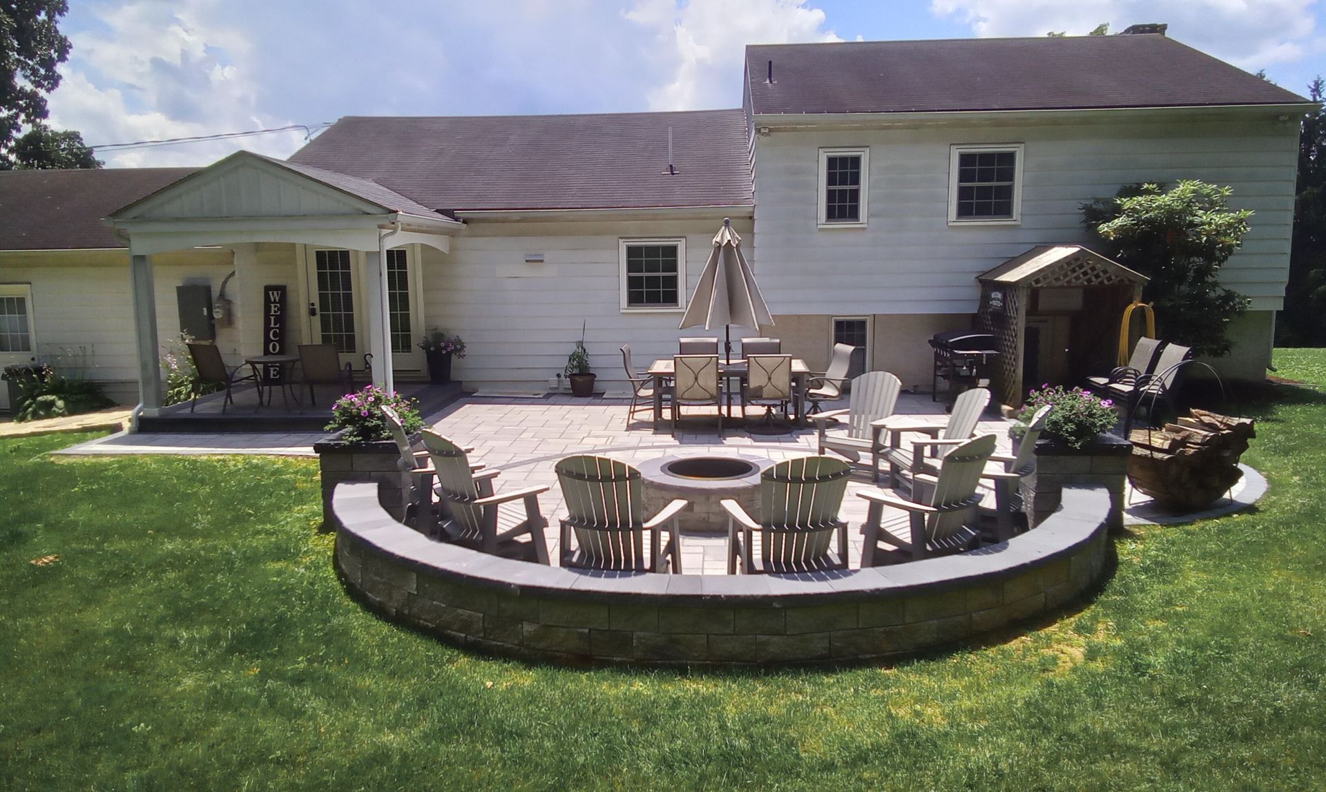 Backyard patio with curved stone fire pit, outdoor seating, lawn, and a white house in the background
