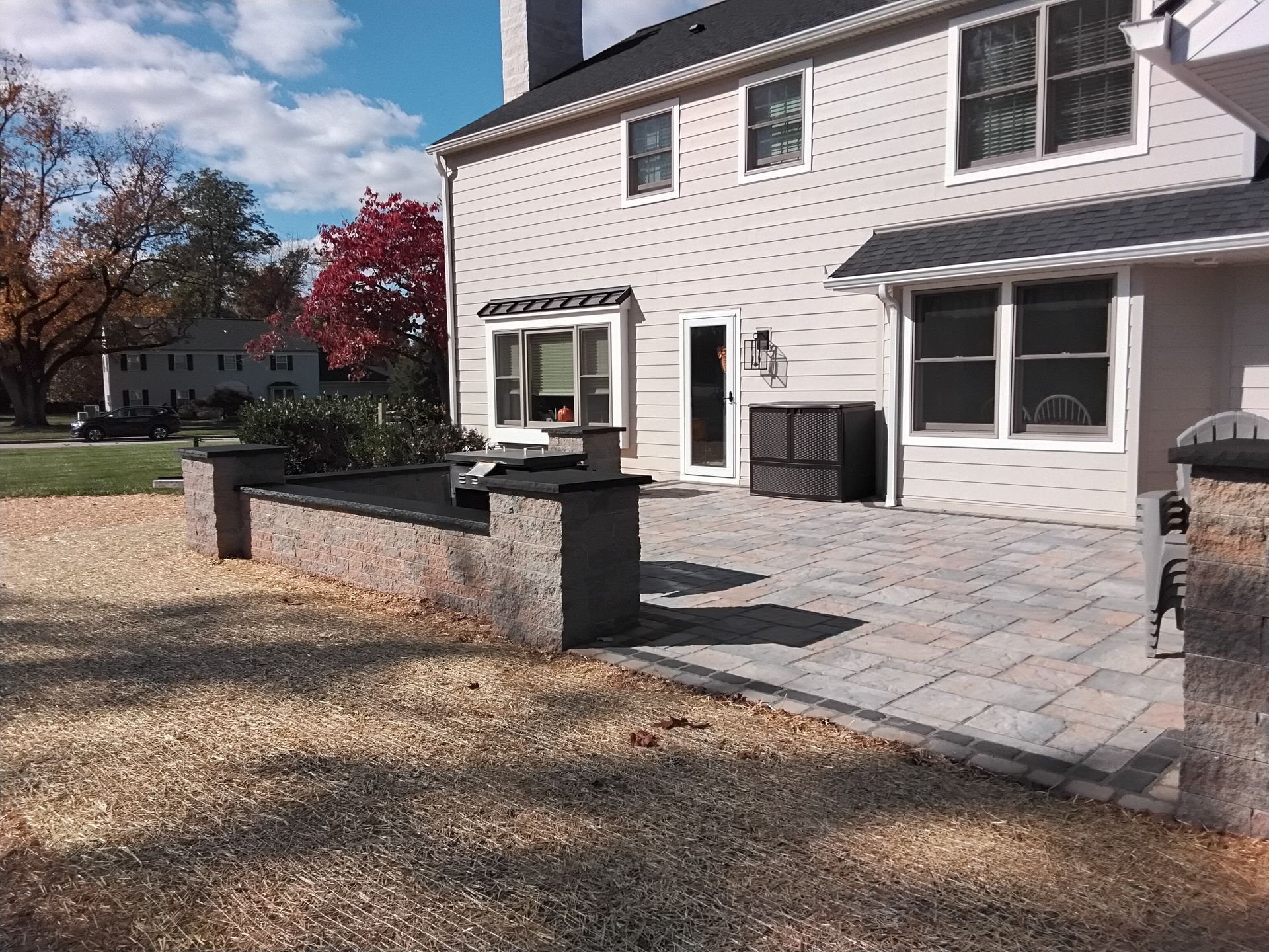 Backyard patio with gray stone pavers, low brick wall, and a white house with sliding doors and windows