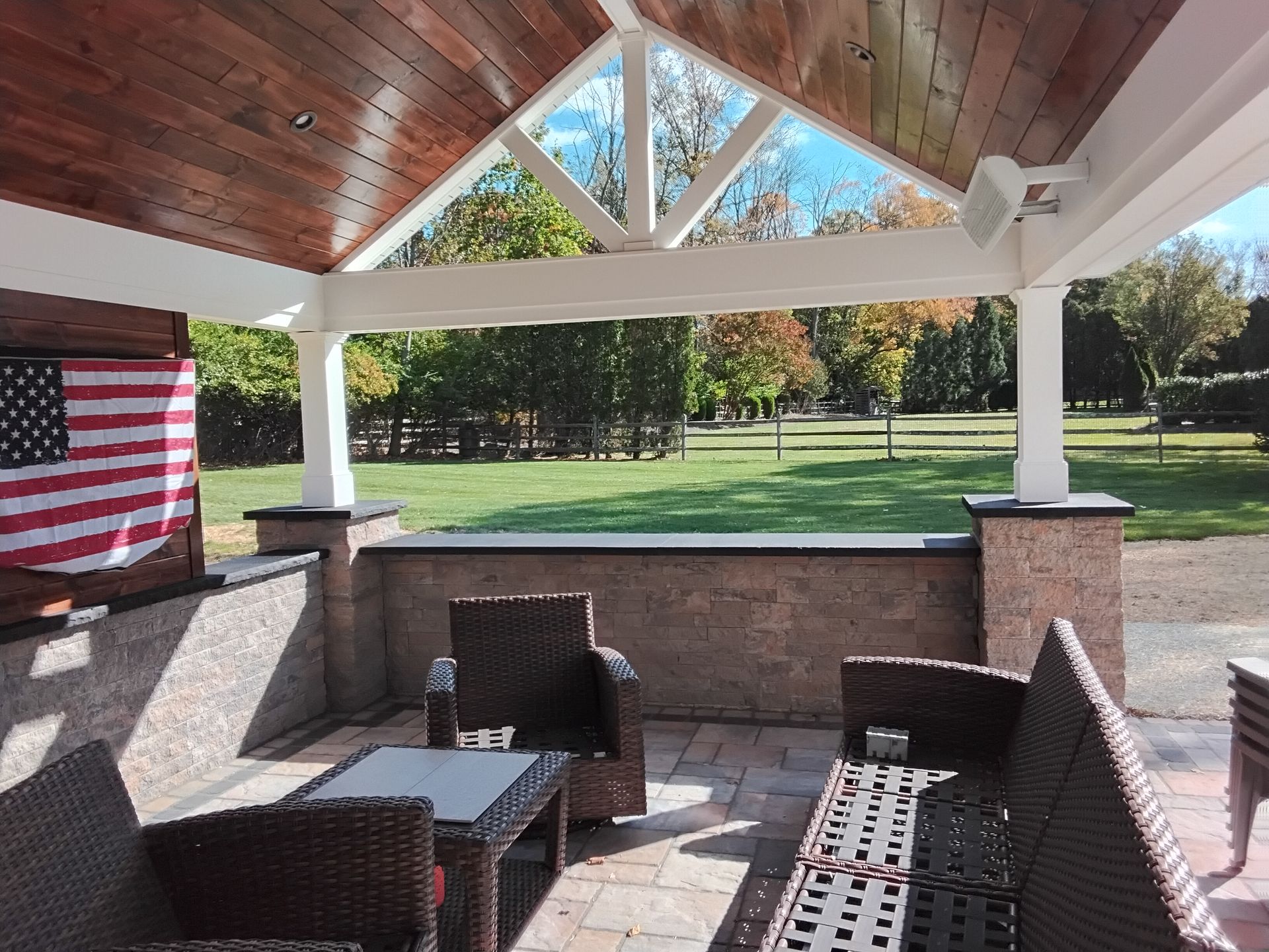 Covered patio with wicker chairs and American flag, overlooking a grassy yard and trees