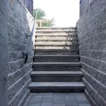 Stone stairs leading up, flanked by stone walls, with a handrail on the left.