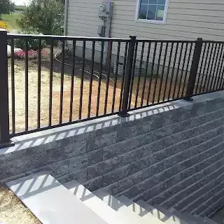 Black metal fence atop a retaining wall with steps, next to a house with a window.