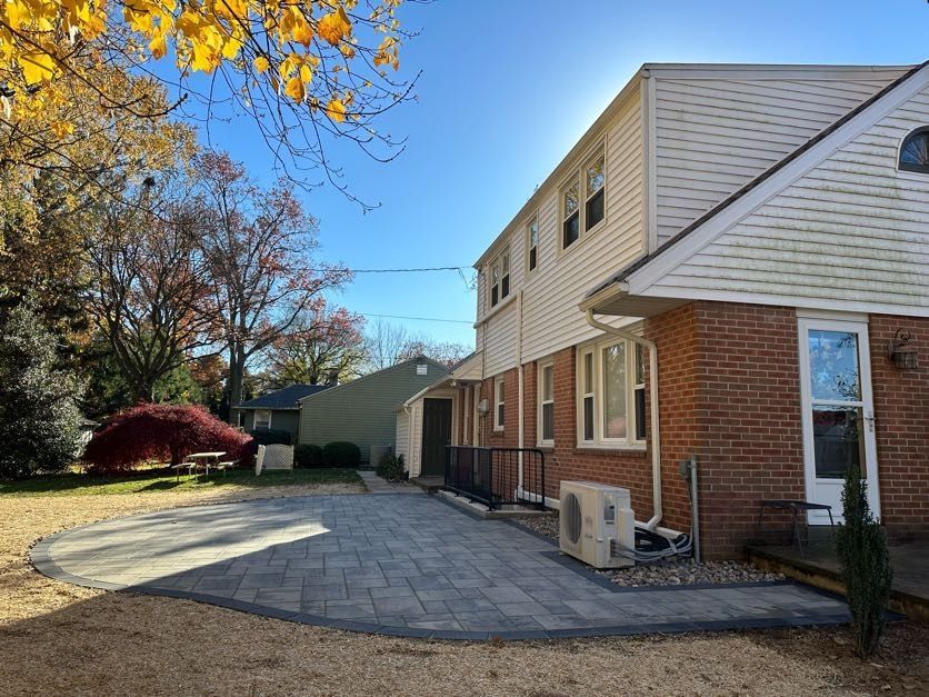Brick house with white siding and patio, viewed from a paved driveway beside autumn trees.