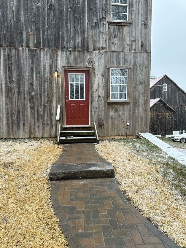 Red door on weathered wooden building with steps, brick walkway, and snow on the ground