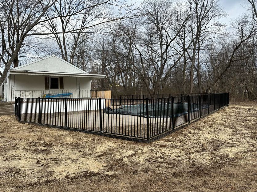 Black fenced backyard with an above-ground pool beside a small house and leafless trees.