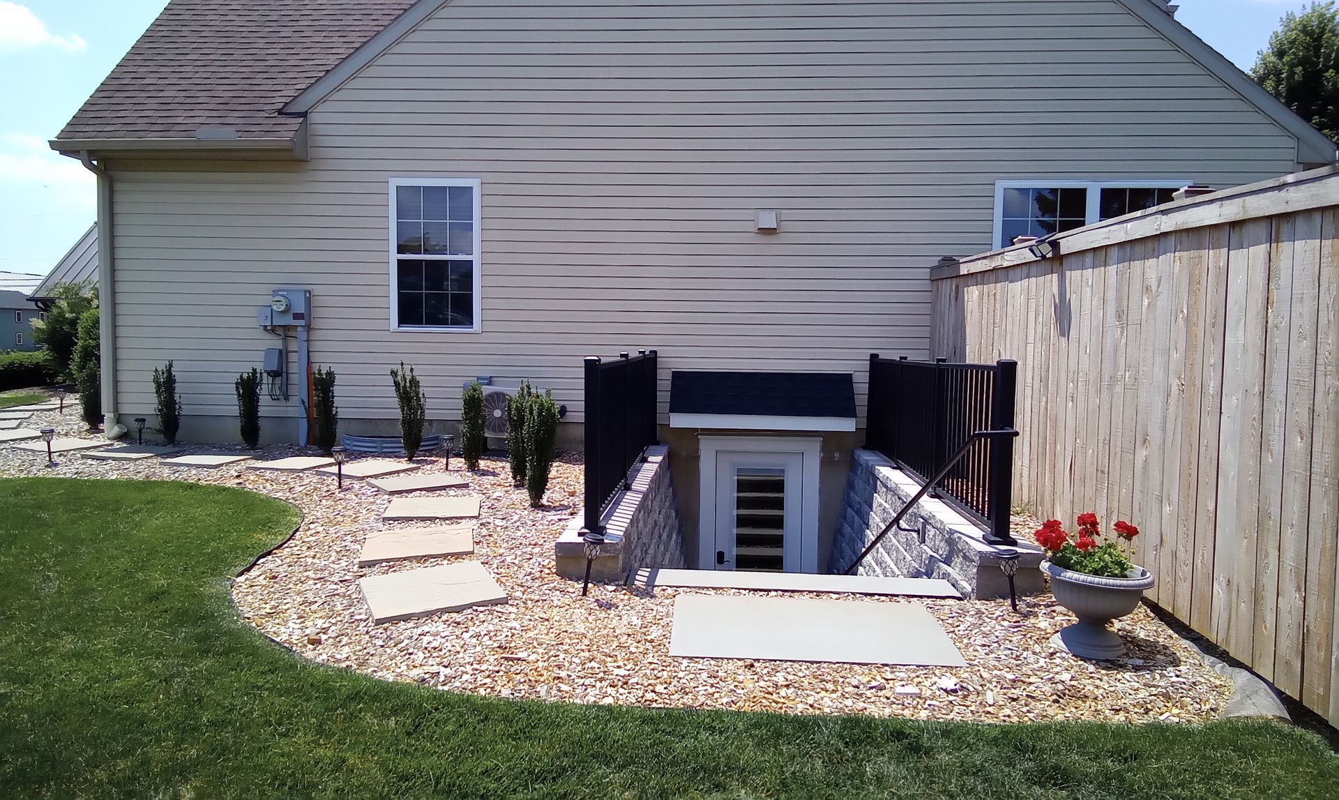 Exterior view of a house with a basement access, stone path, and wooden fence.
