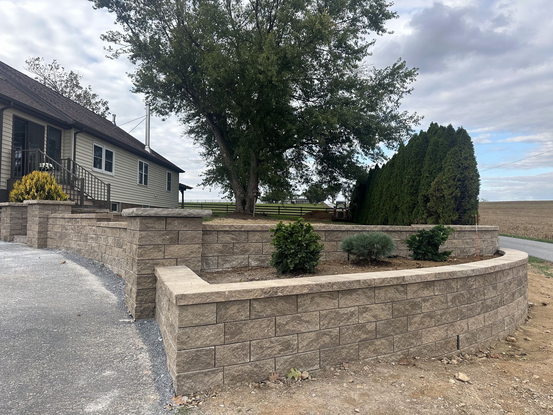 Low retaining wall with landscaping next to a house and gravel driveway.