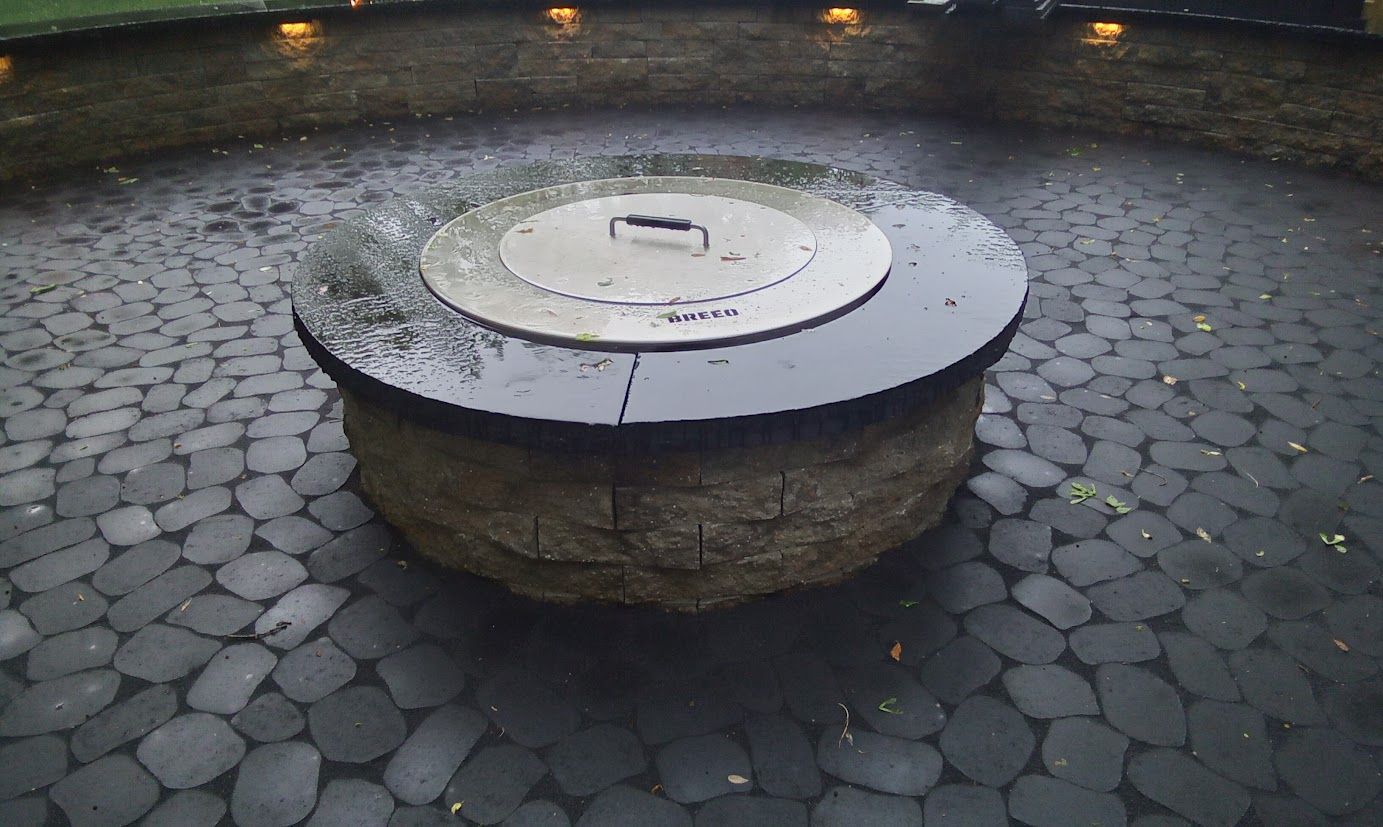 Stone fire pit with a metal lid on a cobblestone patio.
