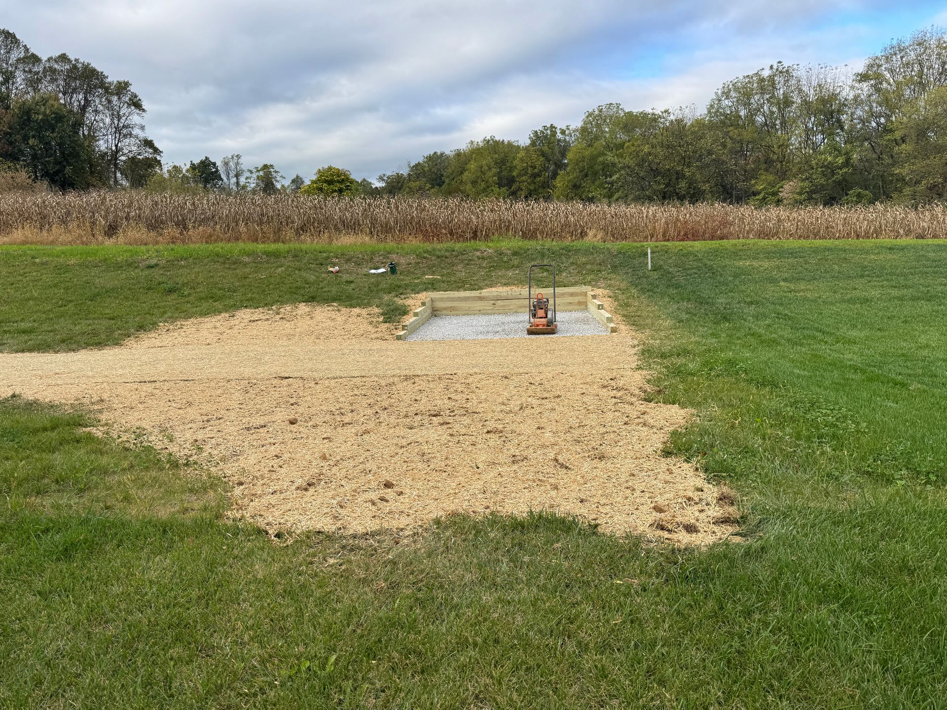 Gravel patch with an orange pump near a green lawn; trees and cloudy sky in the background.