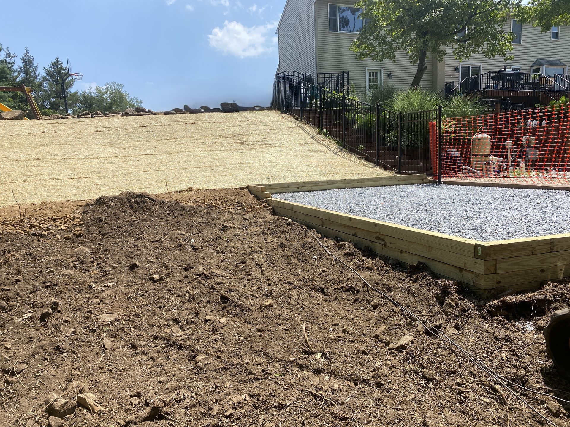 A backyard with freshly laid dirt, gravel, and a slope with erosion control netting. A house and fence are in the background.