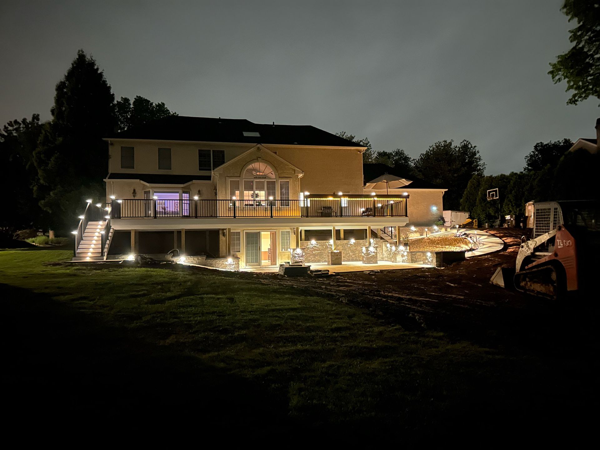 Large house lit up at night with string lights and a pool in the backyard