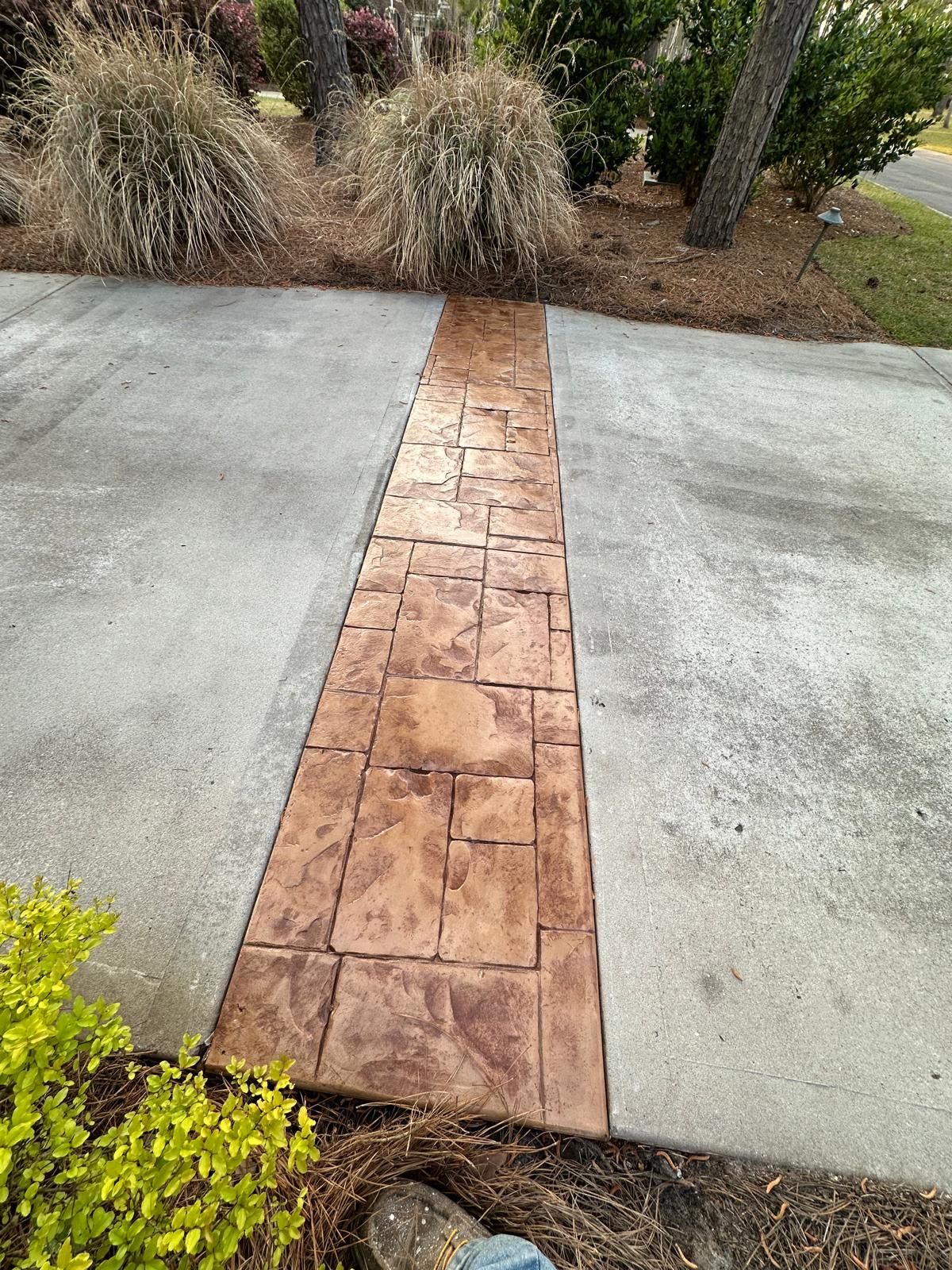 Concrete walkway with a narrow reddish brick strip leading into a landscaped garden area
