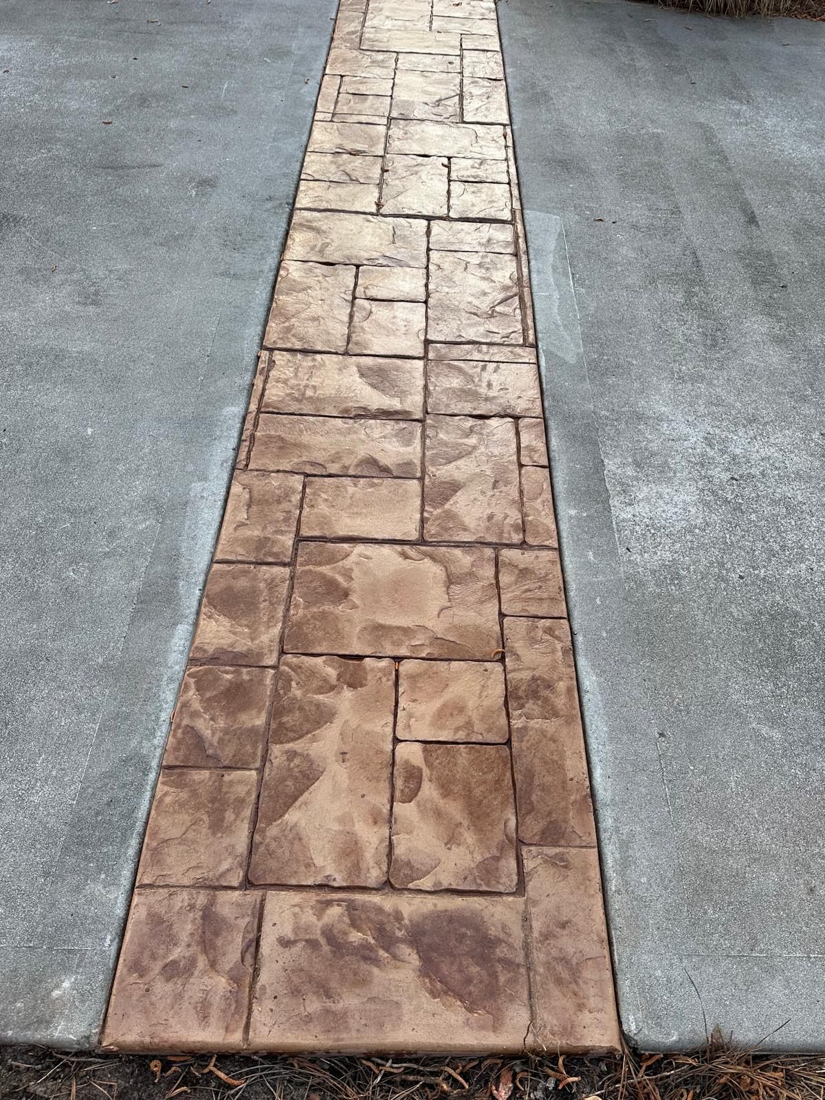 Narrow stamped concrete walkway between two gray pavement strips