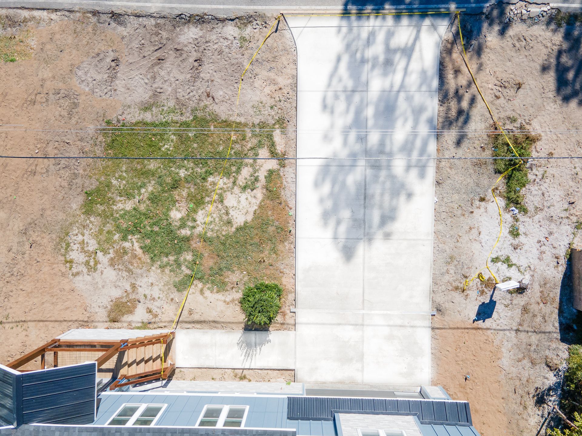 Overhead view of a dirt lot with a concrete walkway, patchy grass, and a small building edge at bottom left