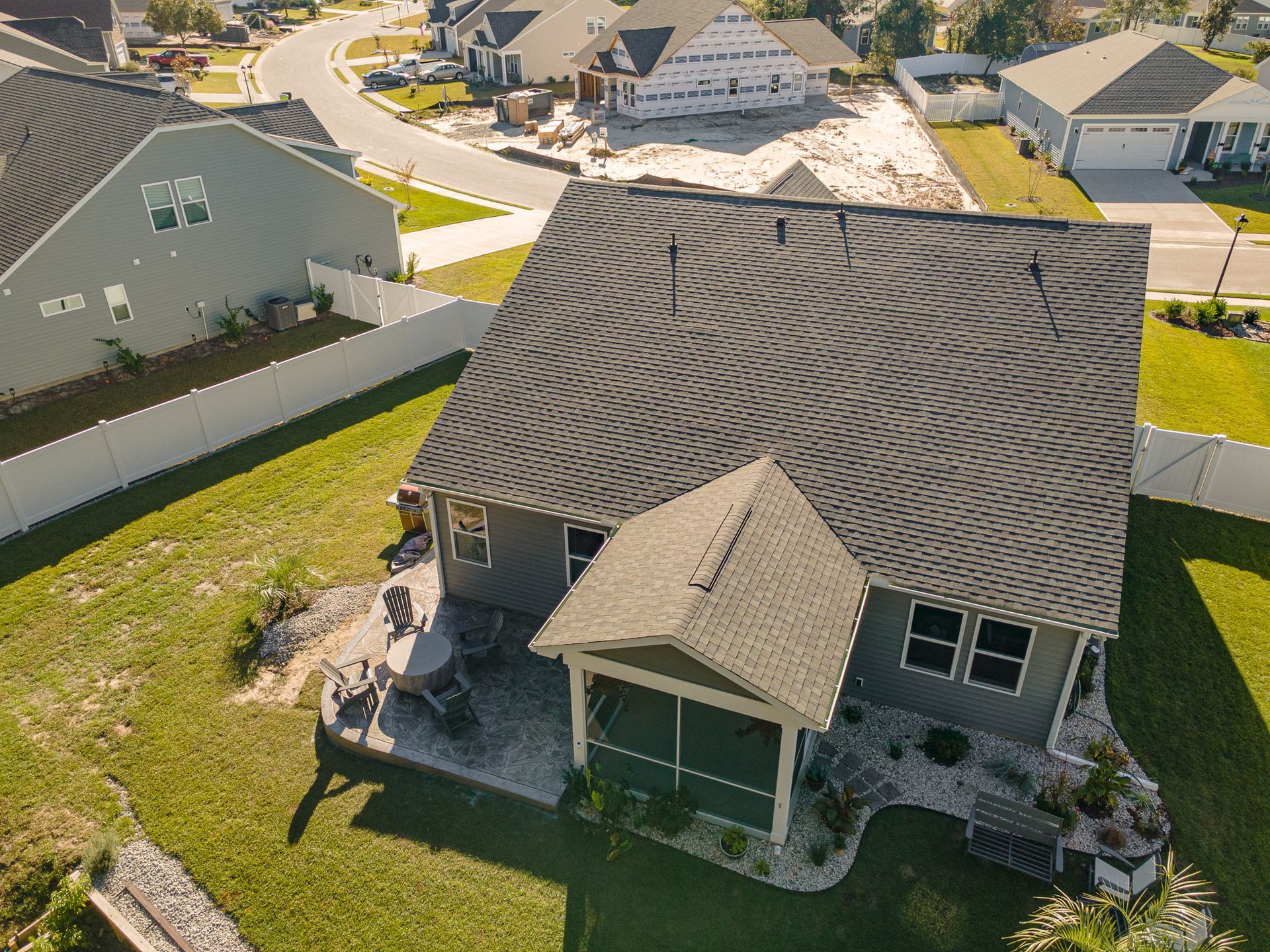Aerial view of a suburban house with a dark shingle roof, front porch, and neighboring homes nearby