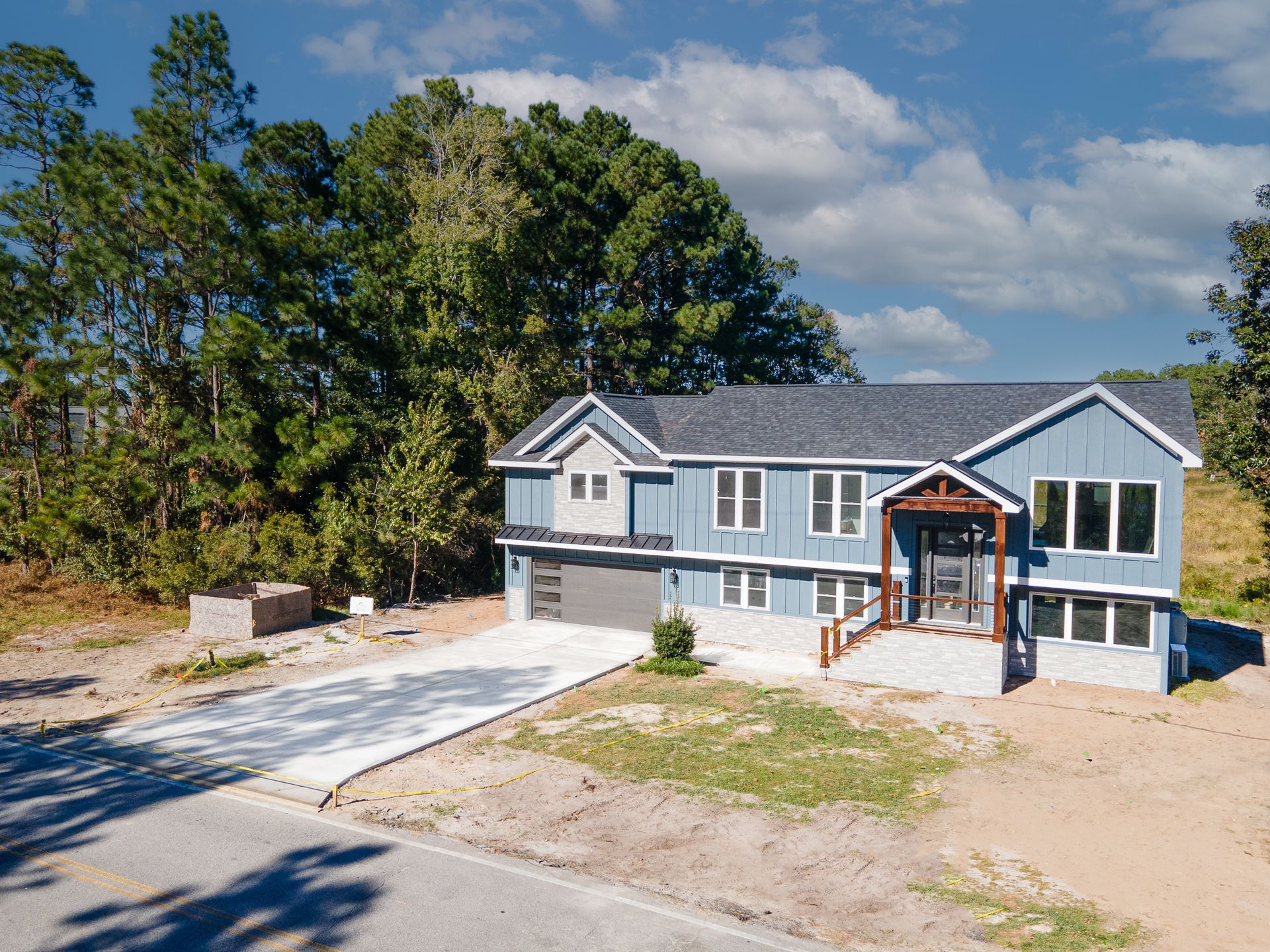 Two-story gray house with white trim, front porch, and unfinished yard under a blue sky