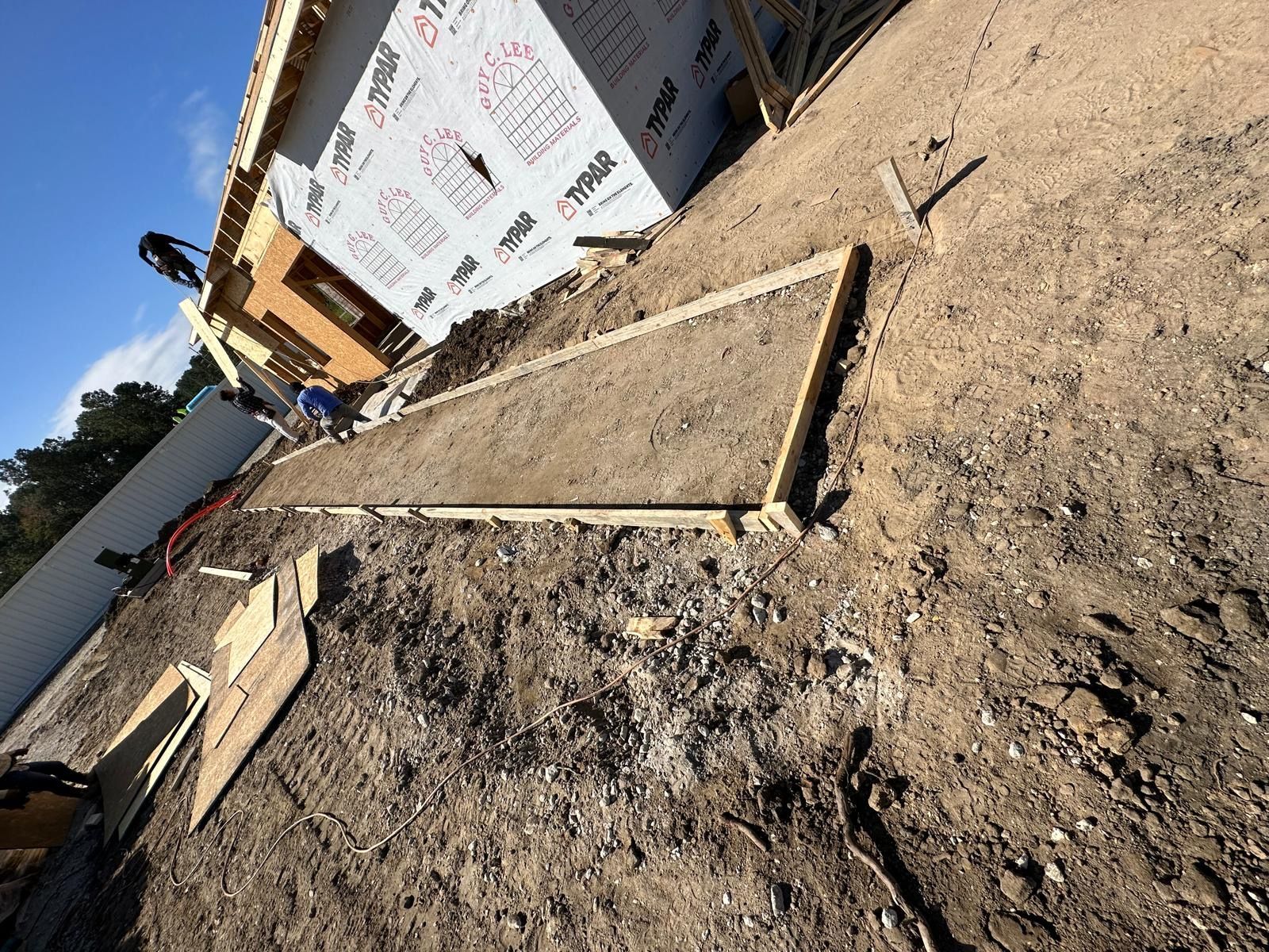 Tilted view of a construction site with concrete footings, dirt, and a building wall with posted signs