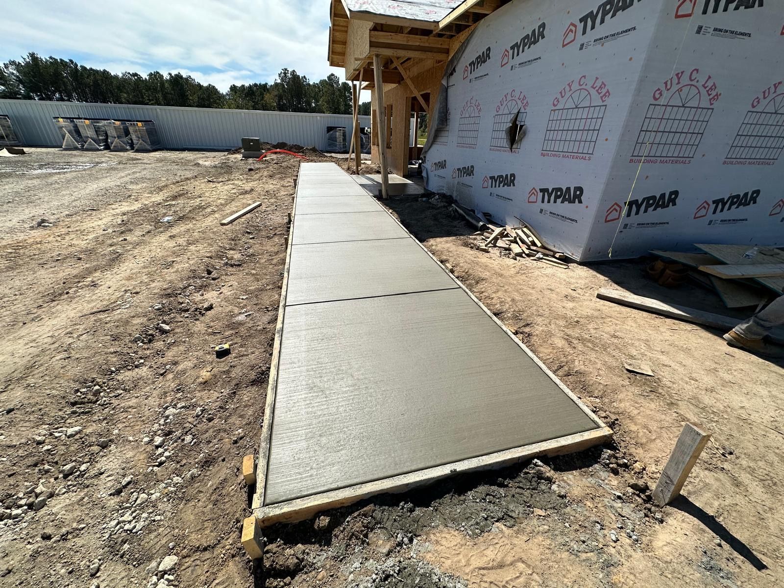 Freshly poured concrete walkway beside a house under construction on a dirt lot