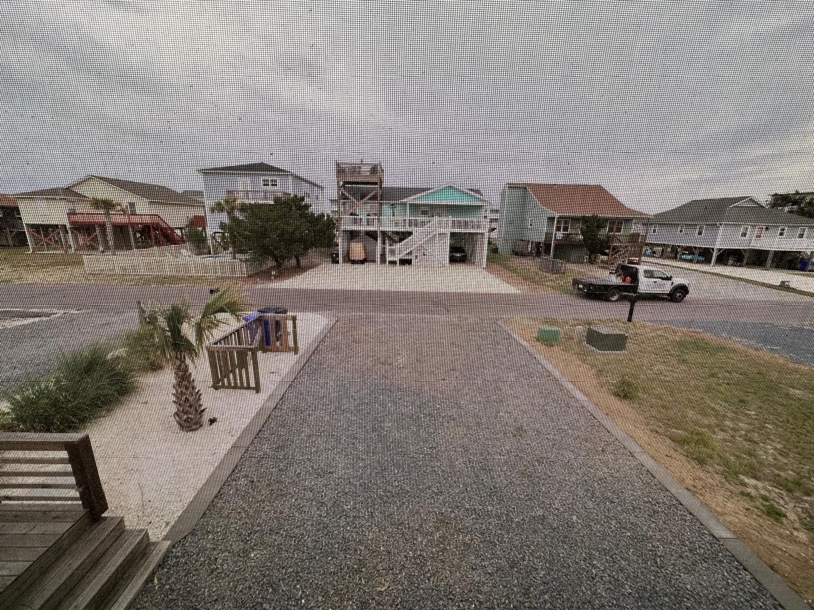 Wide gravel path leading to a plaza with trees, benches, and buildings under a cloudy sky