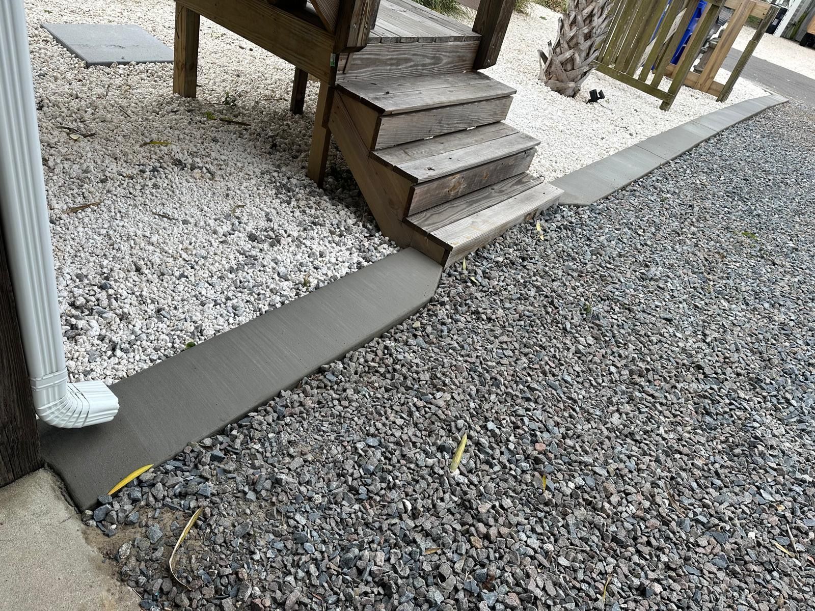 Gravel yard beside a wooden deck stairs, with a concrete path and white gravel border.