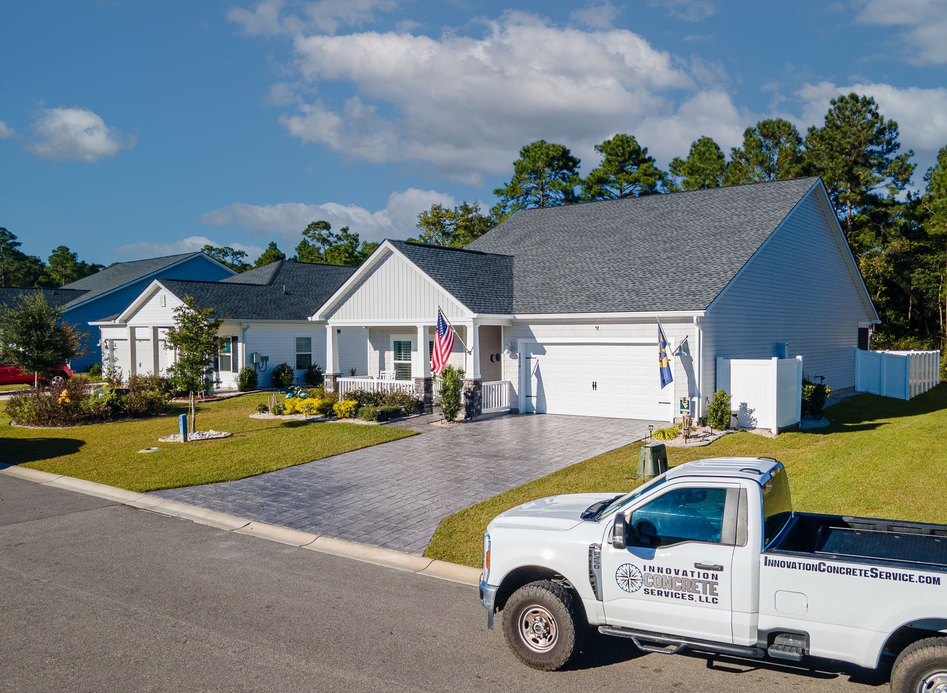 Suburban houses with gray roofs, one displaying an American flag, and a white utility truck parked in front