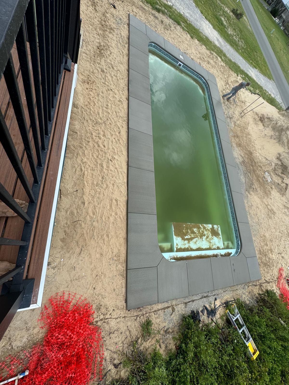 Outdoor rectangular pond with green water beside a building and gravel path