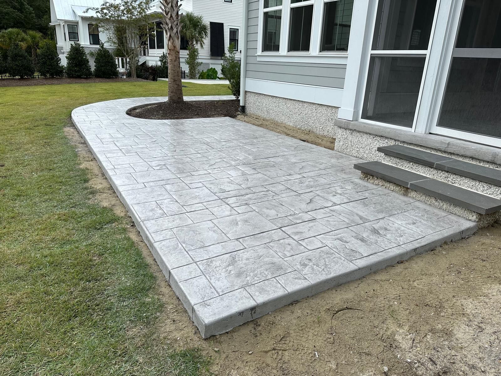 Stamped concrete patio beside a house, with steps and a small tree planter.
