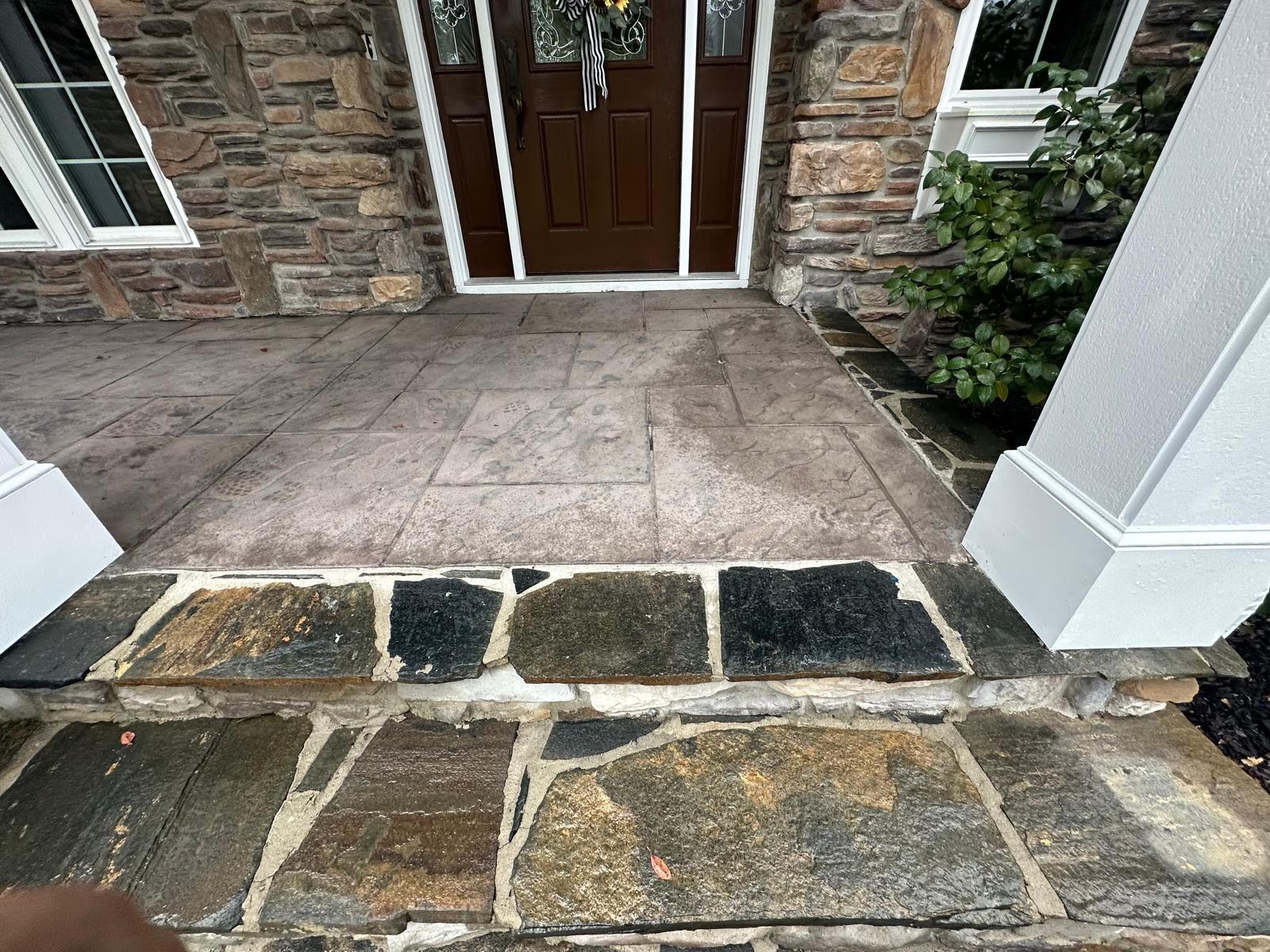 Stone front steps leading to a brown front door with white trim and a paved entryway