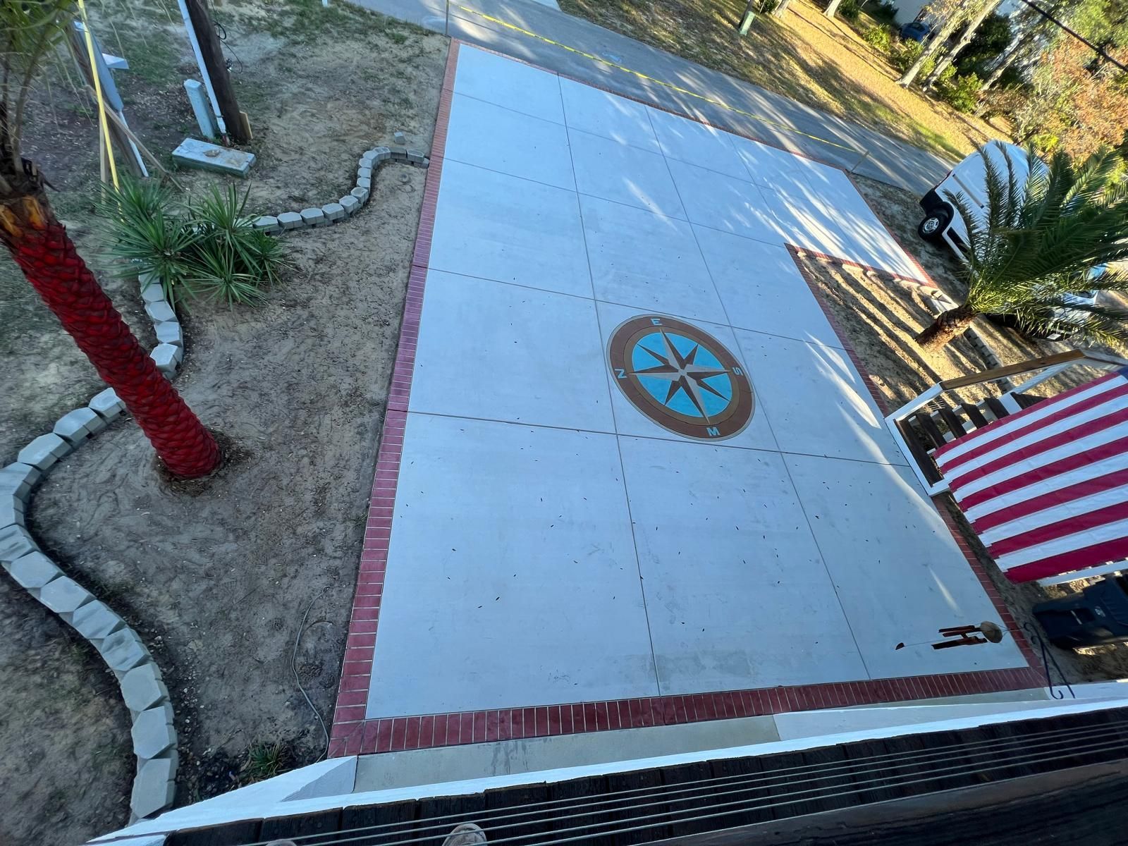 Tilted view of a concrete slab with a compass rose, bordered by red brick and a striped barrier nearby