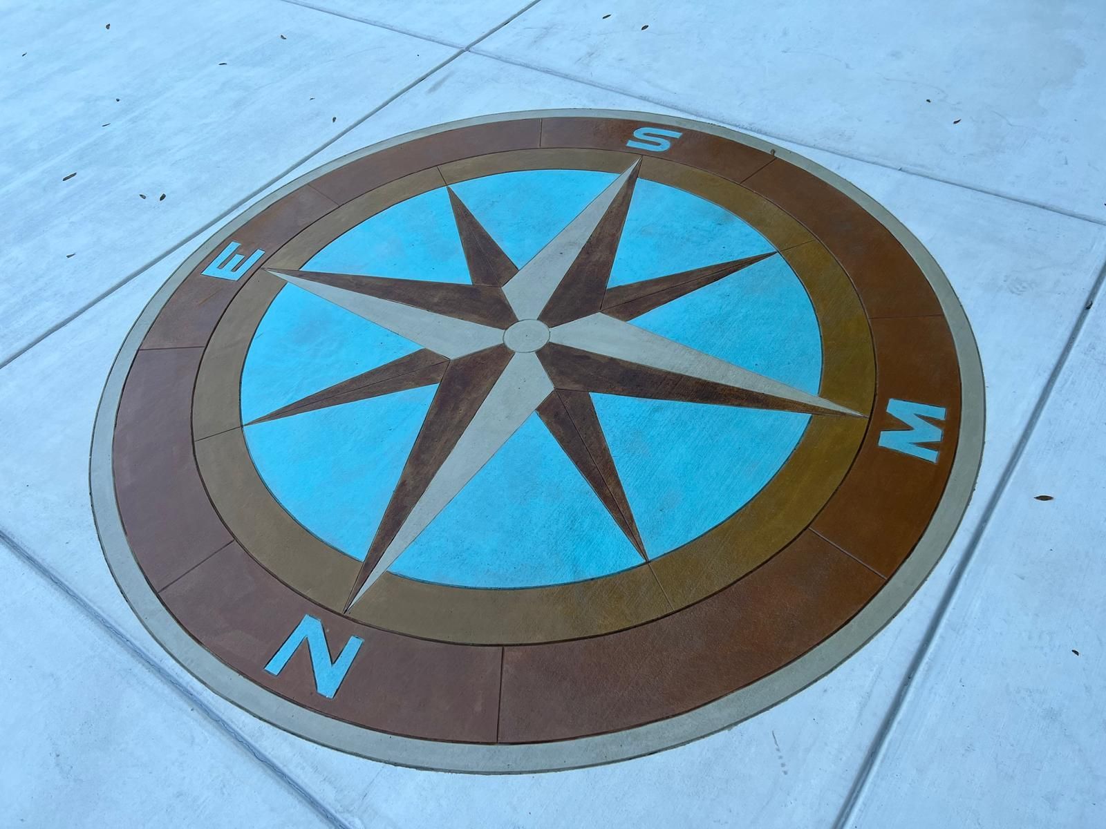 Compass rose painted on pavement with N, E, S, and W directions in blue and brown.