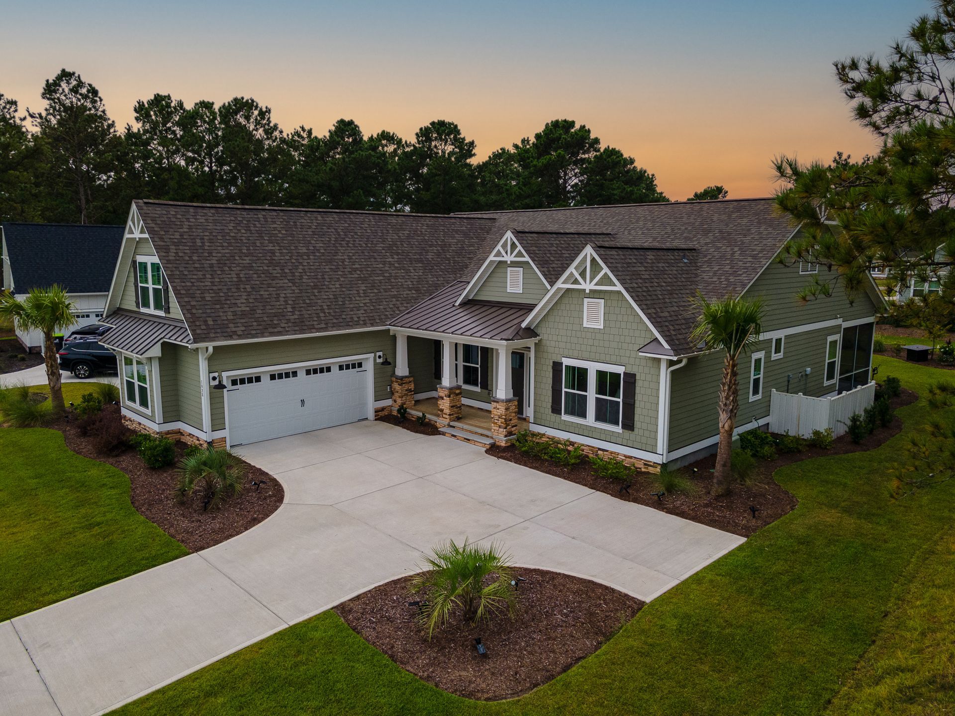Aerial view of a gray suburban house with a two-car garage, curved driveway, and landscaped front yard at dusk