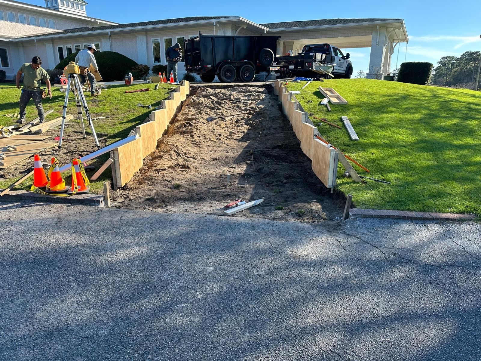 Front yard driveway under construction with an excavated ramp, dirt, orange cones, and a house in the background