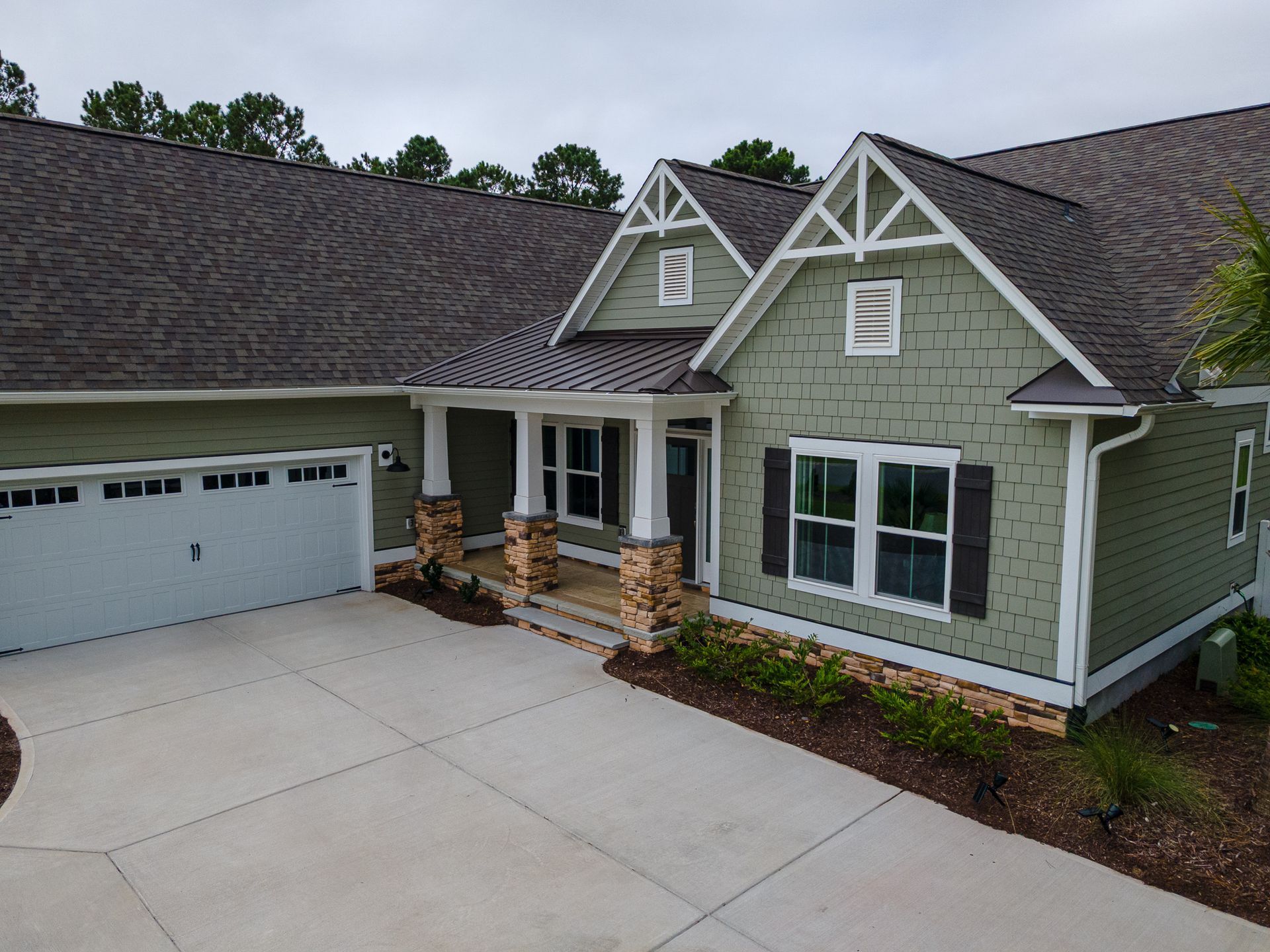 Front view of a green suburban house with white trim, two garage doors, and a concrete driveway